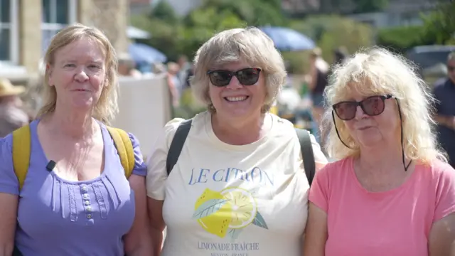 Lynne Sawyer, Debbie Saxby and Carol Alder, who are standing outside Westleton Village Hall. They are all smiling. Lynne is wearing a purple T-shirt, Debbie a white T-shirt and Carol a pink T-shirt.