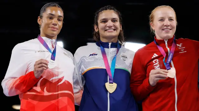 Chantelle Reid, far left and wearing England's white and red tracksuit jacket, holds up her silver medal. Rosie Eccles, second right and wearing Wales red jacket, holds up her bronze.