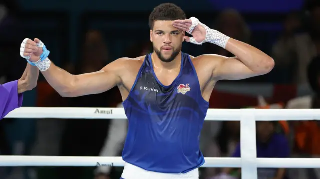Damar Thomas, wearing England's blue jersey, salutes while his hand is held up to celebrate winning gold