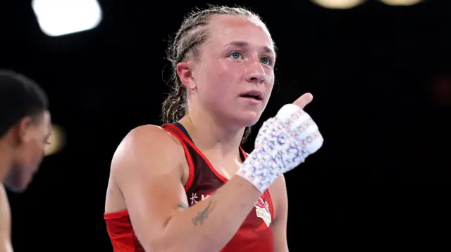 Ruby White, wearing England's red jersey, holds up her hand to celebrate victory on the round of 16 fight against Thandolwethu Truelove Mathiba