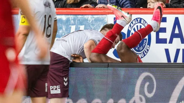 Hearts' Stuart Findlay helps Aberdeen's Toyosi Olusanya after a fall over the advertising hoardings