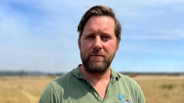 Tom Martin, a man with short brown hair and a brown beard. He is wearing a green T-shirt, looking into the camera.