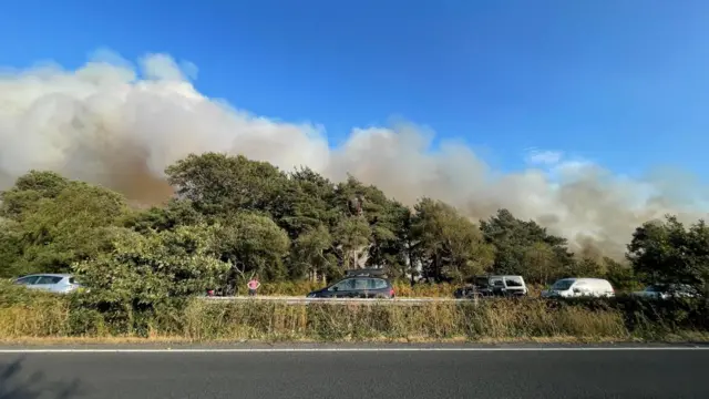 A group of vehicles a short distance away pictured in front of smoke rising from heathland.