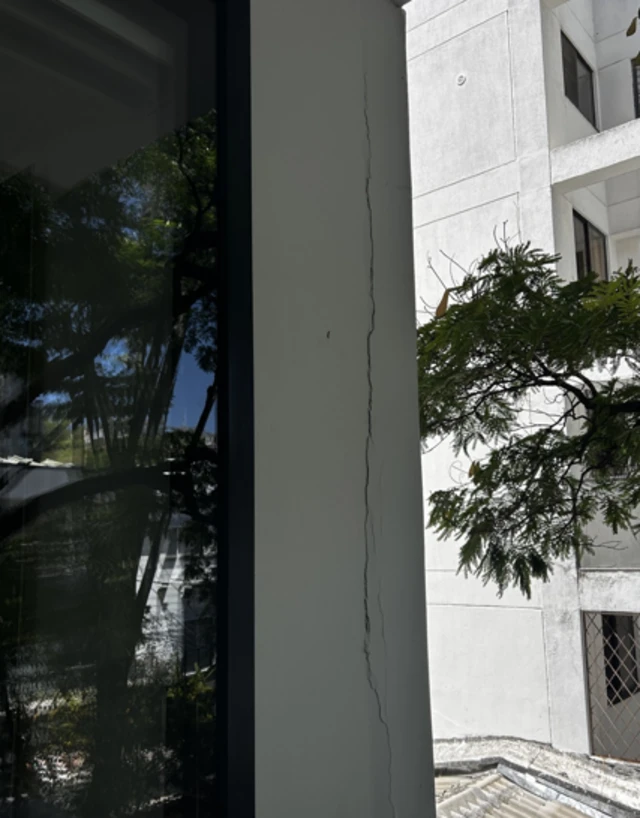 A long crack is seen down a white wall next to a window