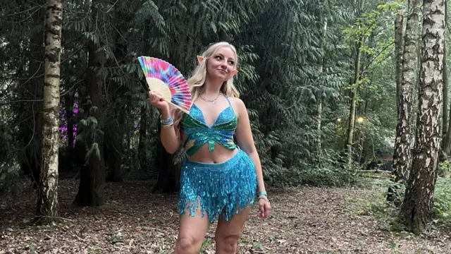 A young woman poses with a fan in a wooded area