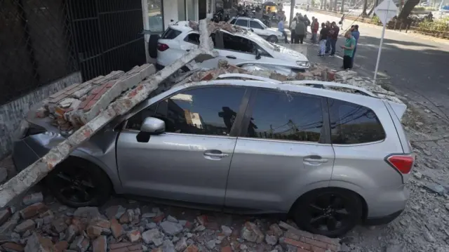 Brickwork is shown collapsed onto a row of parked cars against a building.