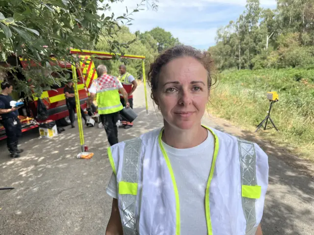 Vicky, a women in a white T-shirt and a green and white high-visibility jacket, looking into the camera.