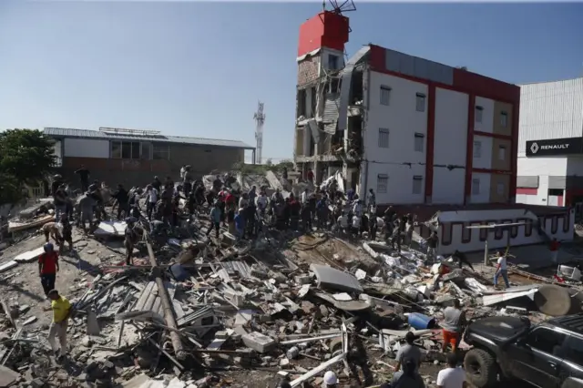 People walk through the rubble of a collapsed building
