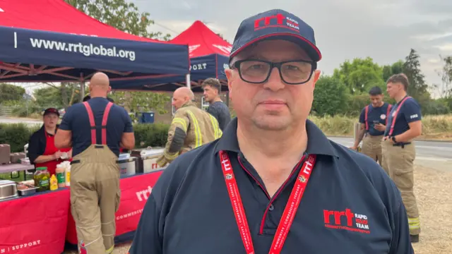Graham, a man in a blue T-shirt. He is wearing a blue skull cap and a red lanyard, looking into the camera.