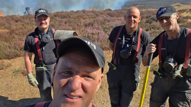 A selfie of four firefighters in front of burning vegetation
