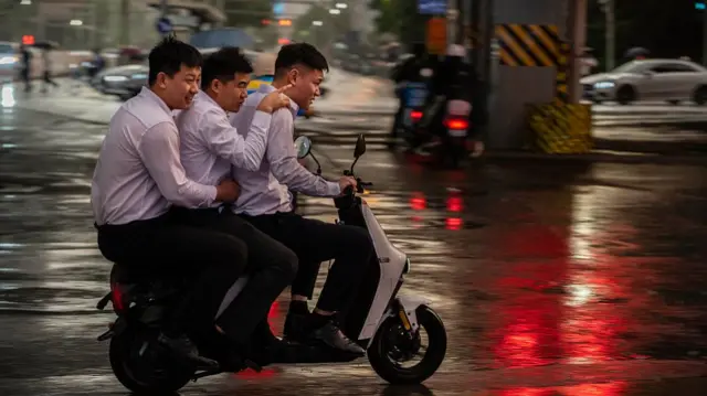 three men wearing white formal shirts and black trousers are cramped on a motorbike in Beijing China under heavy rain