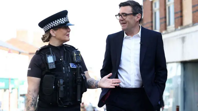 Britain's Prime Minister Andy Burnham (R) talks with a police officer as they walk past shops in the town centre of Ilkeston, Derbyshire, central England on August 11G