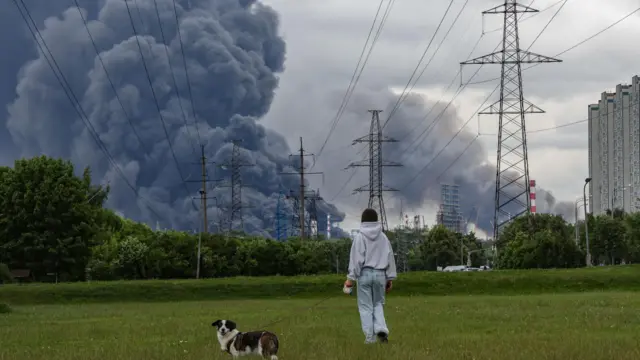 A woman walks in a park as smoke billows in the background following a reported Ukrainian drone attack, in Moscow, Russia, 18 June 2026.