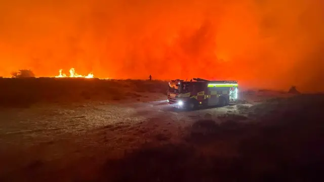 A fire engine at night in a bright red landscape, caused by the reflection of flames on clouds of smoke