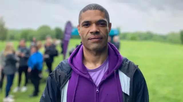 Calvin Buckley poses for the camera wearing a purple hoodie and black jacket