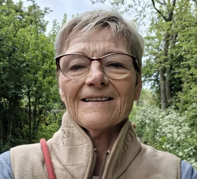 A woman with short hair and a gilet stands in a forest