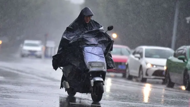 Man wearing a black raincoat rides a scooter under typhoon rains in China