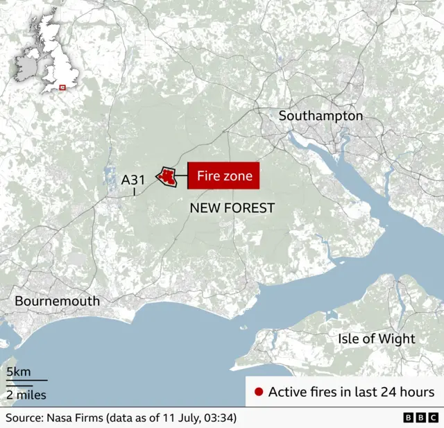 Map of the New Forest area in southern England showing the location of a wildfire near the A31 road, west of Southampton and east of Bournemouth. A red highlighted area labelled “Fire zone” marks the affected section of the New Forest. Red dots indicate active fires detected in the last 24 hours, including two near Southampton Water. An inset map of the UK in the top left shows the fire’s location in southern England. The map includes a scale bar and cites NASA FIRMS data as of 11 July, 03:34.