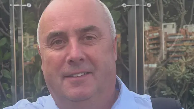 Phil Hannat, a white man wearing a blue shirt and looking at the camera.