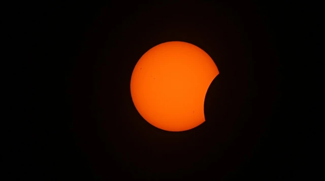 Bright orange Sun against black sky with a small notch taken out on left hand side