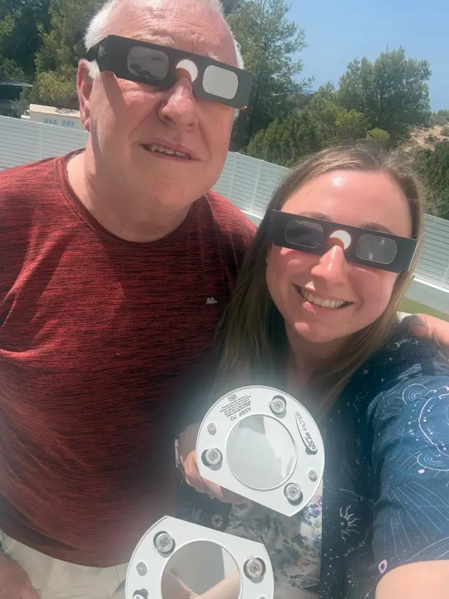 Jenifer Millard smiling with her dad as they hold their eclipse equipment