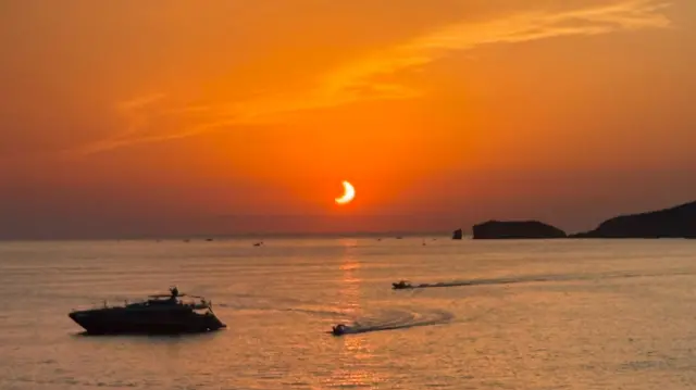 The eclipse seen over the Ibiza sea with a boat in the foreground