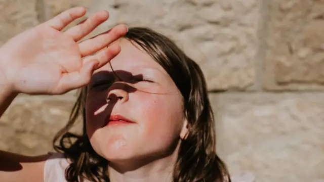 A young girl with brown hair covers her eyes from the sun