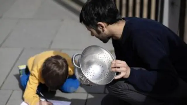 A man and young boy look at a piece of paper as a colander projects the eclipse onto it