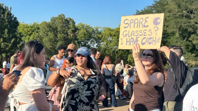 Woman holding up a sign that says "spare glasses, I have cash"