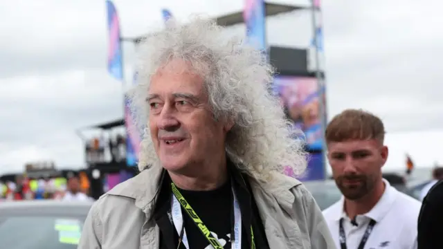 Queen's Brian May looks to his right as he walks through Silverstone