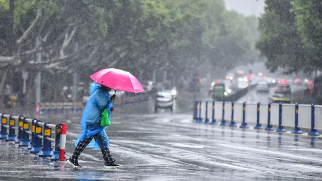Person wearing blue rain coat and pink umbrella walking under wind and rain in Fuyang City, Anhui Province, China