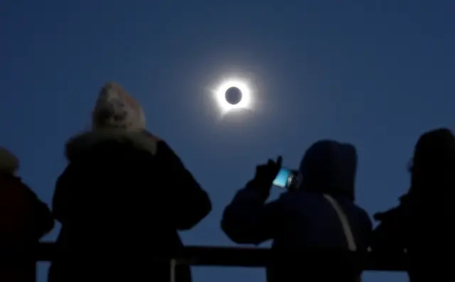 People silhouetted taking phone images of the full eclipse