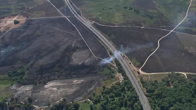 An arial view of charred land in the aftermath of the wildfire in the New Forest. Smoke is rising from the burned land.