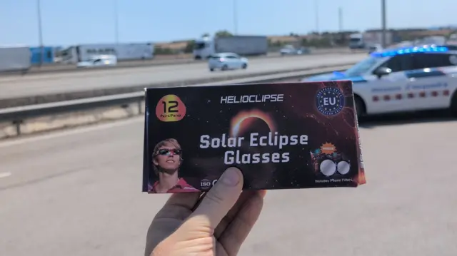 A hand holding out a pair of eclipse glasses on a Spanish motorway north of Barcelona