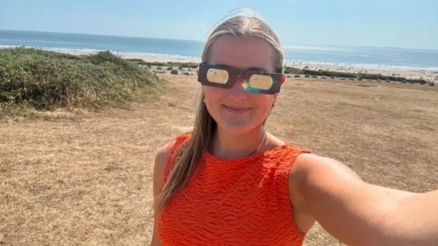 BBC Reporter Eleri Griffiths wearing eclipse glasses on a beach in south Wales