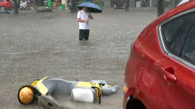 A man shelters under an umbrela while standing in knee-deep floods in Taizhou, Zhejiang province