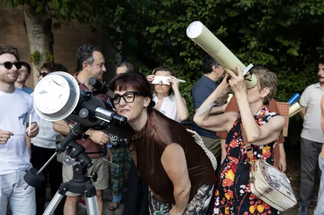 People with telescope and pinhole tube in crowd