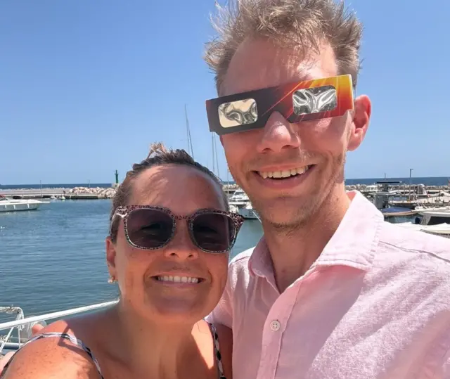 BBC reporter Kris Bramwell wearing eclipse glasses with his partner Holly on holiday in Mallorca