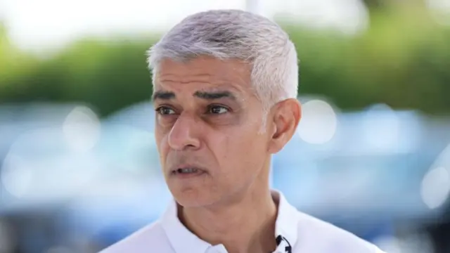 Sadiq Khan in a white shirt stands outside