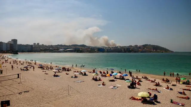 Smoke rises from a forest fire as people gather at Orzan Beach ahead of a solar eclipse in A Coruna in Galicia, Spain