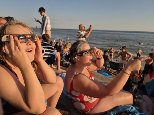 A young child and a woman look shocked as the point towards the distance while wearing their sunglasses
