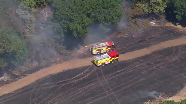 An arial shot of two fire engines tackling fire at a field. There is smoke coming off the burnt ground.