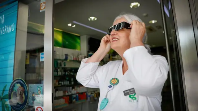 A pharmacist tries on glasses for the solar eclipse at her pharmacy in Pamplona, Spain