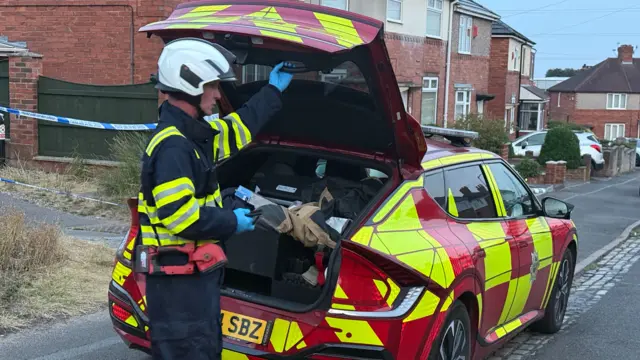 A firefighter at the back of a fire car with the boot open, reaching to pull it down.