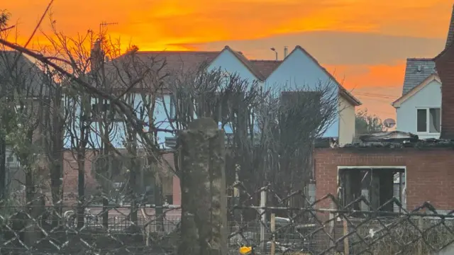 A fire-damaged home beyond a fence.