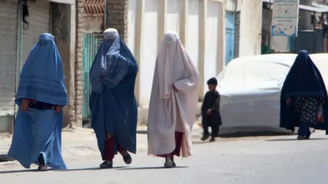 Four women dressed in burqas that cover their whole bodies are shown walking down a street in Afghanistan.