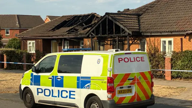 A building with a collapsed roof is just behind a van with police written on the side.