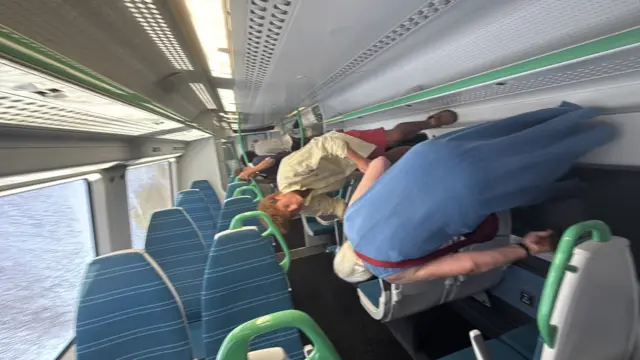 People stand on the walls of a train, seats and windows above their heads. The windows are cracked.