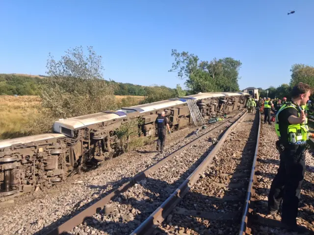 A derailed train by the side of tracks. It has tipped into a field.
