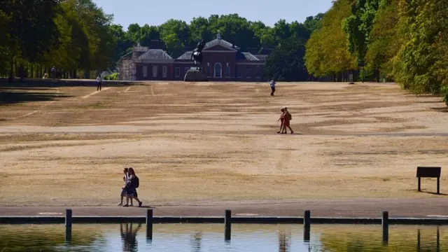 People walk on dry grass in Kensington Gardens